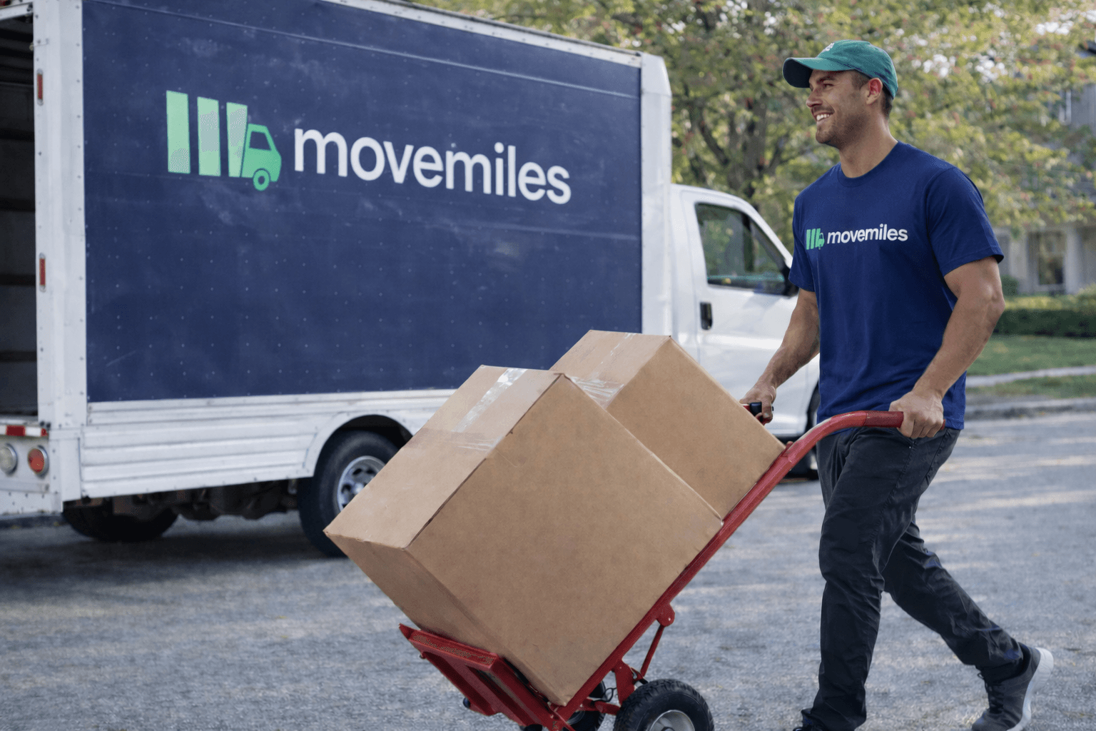 Movemiles mover walking a dolly of boxes next to a Movemiles truck